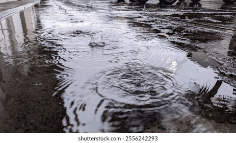 Raindrops create ripples on a puddle, reflecting buildings and vehicles. Captured at ground level, this urban shot blends textures, light, and reflections, evoking calmness and beauty in everyday mome