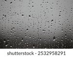 Raindrops in different sizes on window with gray background. Raindrops falling on glass.