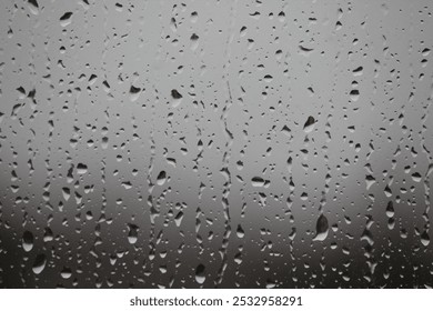 Raindrops in different sizes on window with gray background. Raindrops falling on glass.