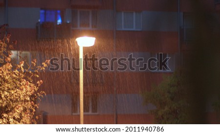 Raindrops fall against the background of a lantern in the courtyard of the house. The light of lightning is blinking on the facade of the house. Night rain gives freshness in summer.