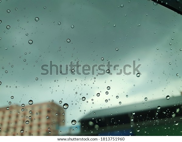 Raindrops fall by the window\
of a car driving on the road in the rain and a cloudy sky in the\
evening.