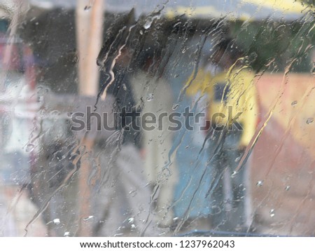 raindrops fall on a dusty car window, blurred persons and colorful streetlife can be seen outside - can be used as background