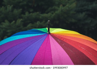 Raindrops fall from the sky onto a rainbow-colored umbrella. Light rain. Cloudy weather.