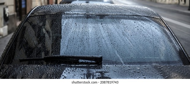 Raindrops On A Back Car Glass. On A Cloudy, Rainy Day, The Back Window And Windshield Wiper Of A Car Are Covered With Drops Of Torrential Rain. Sadness. Melancholy. Bad Weather.