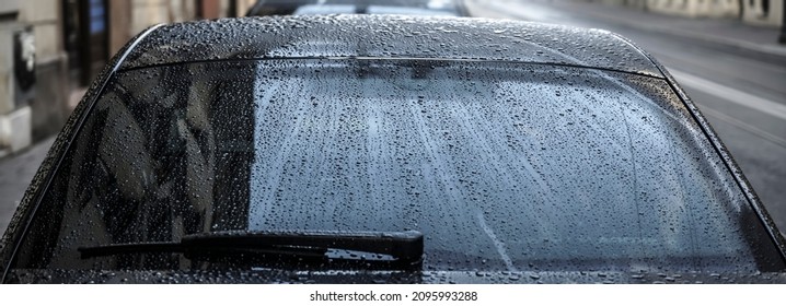 Raindrops On A Back Car Glass. On A Cloudy, Rainy Day, The Back Window And Windshield Wiper Of A Car Are Covered With Drops Of Torrential Rain. Sadness. Melancholy. Bad Weather.