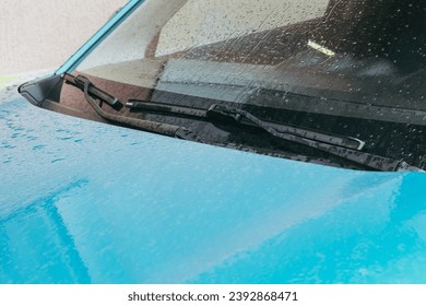 Raindrops on the car. Car element with raindrops close-up. The hood, mirror and glass of a blue car covered in raindrops. Big raindrops on the car very close