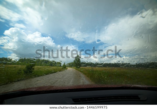 Raindrops on the car window. Rural landscape.
Summer rain. Dirt
road.