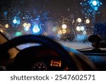 Raindrops on a car windshield with blurred colorful city lights at night, viewed from inside. A steering wheel and dashboard illuminated in soft light