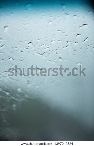 Raindrops\
on a front and side window while car running on the slippery high\
way with a clear sky during a raining\
season.