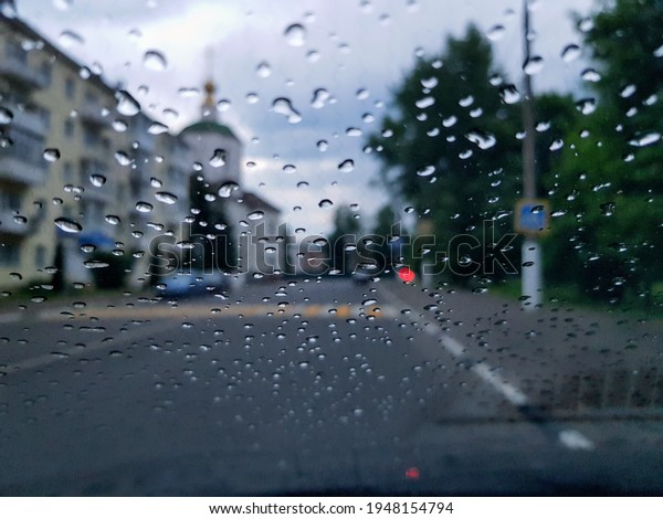 Raindrops on the glass of the car on the\
background of a city street on a cloudy\
day.