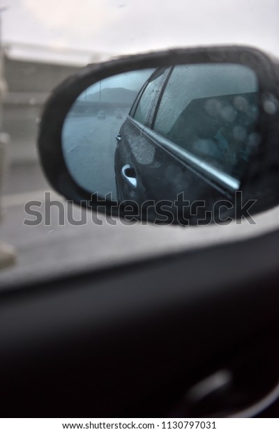 Raindrops on a side mirror and a side window
while car running on the slippery high way with clear sky during a
raining season.