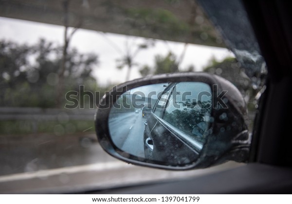 Raindrops on a side mirror and a side window\
while car running on the slippery high way with clear sky during a\
raining season.