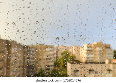 Raindrops on the window against the background of the city during the day. Close up drops on glass on the background of blurry houses. Drops of water on window glass with blur buildings.