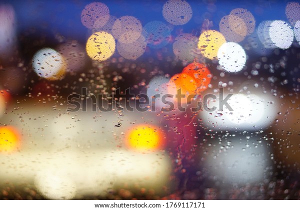 Raindrops on window car with abstract colorful\
bokeh lights of traffic in the night. Romantic in rainy day\
background concept.