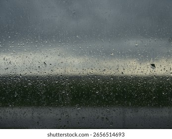 Raindrops on a window with a dark, cloudy sky and blurred landscape in the background, evoking a moody and serene atmosphere.