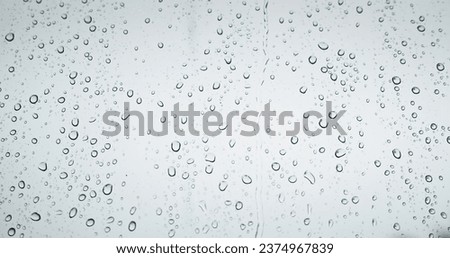 Raindrops on the window dripping down in rainy day autumn monsoon. Gloomy weather drops knock on window glass. Gray natural background.