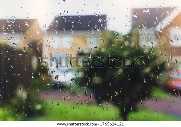 Raindrops on window glass in\
rainy day with blurry tree and house background, View looking\
trough window with water drops texture taken after the rain over\
road background