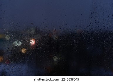 Raindrops on a window glass and unfocused lights of a evening city. Background of night city behind glass during rain, copy space - Powered by Shutterstock