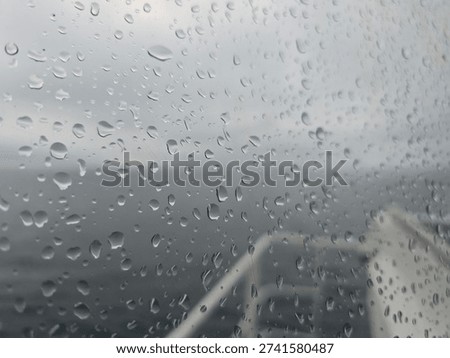 Raindrops on a window pane with a blurred gray sea and ship railing in the background.Abstract maritime background: condensation and rain drops on a glass surface during a storm at sea.View through a wet porthole on a vessel, showing rainy weather and gloomy oceanic horizon.