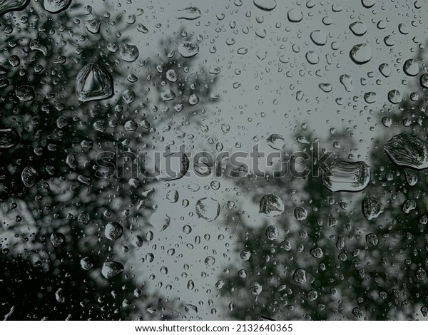 Raindrops on window pane with natural rain on\
cloudy background dark effect in\
forest