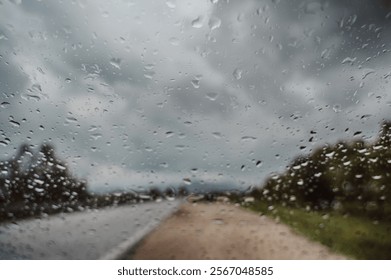 Raindrops on a Windshield Creating a Blurry View of a Countryside Road Under Cloudy Skies on a Rainy Day
