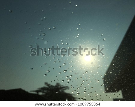 Raindrops on the windshield, the sun is backdrop, car windshield view, blurred background.