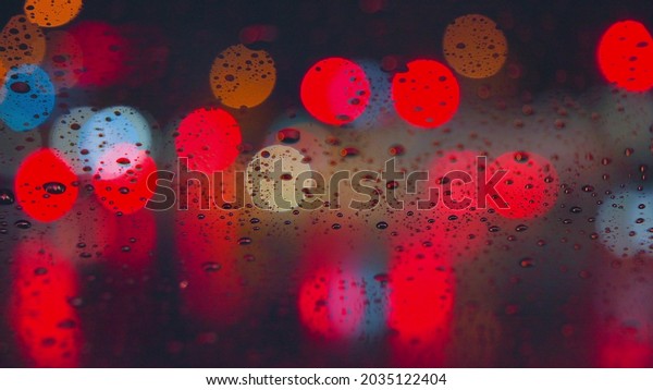 Raindrops run down the\
glass of the car against the backdrop of the bright lights of the\
night city. Rainy night. Cars pass the intersection. Bright colored\
traffic lights