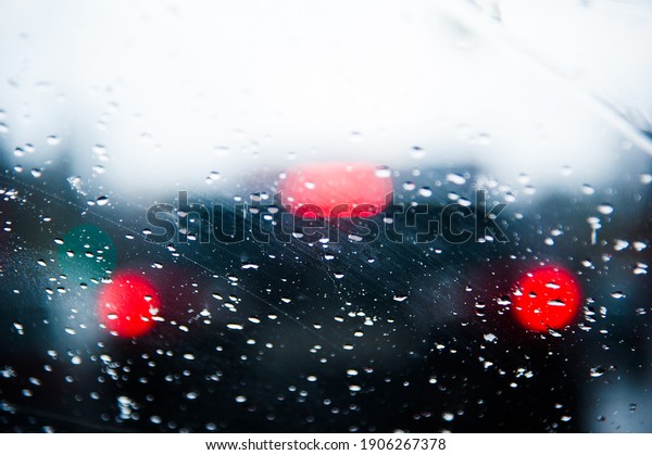 Raindrops run down the windshield of the
car, through which you can see the bright
lights