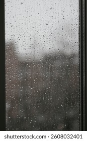 Raindrops slide down a window on a gray, overcast day. The blurred urban background enhances the mood of quiet introspection, evoking a sense of stillness and solitude.