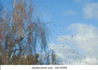 Raindrops splash on window with tree and sky in background