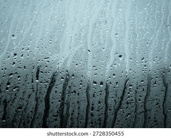 Raindrops trickling down a window pane with moody blue tones
