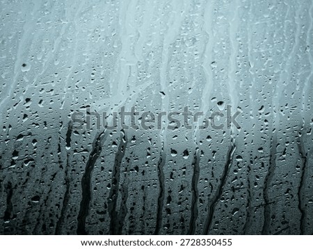 Raindrops trickling down a window pane with moody blue tones