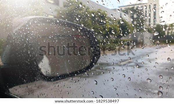 It\'s raining, the car glass is full\
of raindrops with sunlight and slippery wet\
roads.