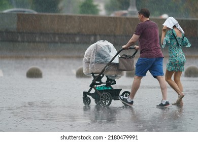 Raining Day In City Center At Summer. Wet Young Family With Baby Pram. Raincoat As Protection. Texture Of Strong, Fresh And Powerful Water Drops And Sprays. Tropical Storm. Backs, Rear View