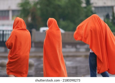 Raining Day In City At Summer. Group Of Young People Walking And Hiding Under Orange Colored Cover. Texture Of Strong, Fresh And Powerful Water Drops And Sprays. Tropical Storm. Backs, Rear View