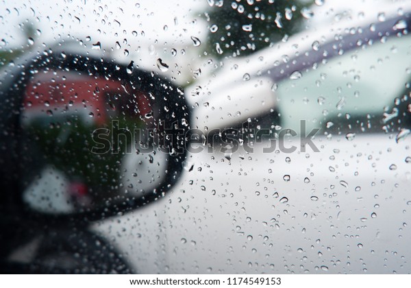 Raining outside the car while driving ,\
rainyday , raindrops on the car glass blur Rain on the car window\
with out side door mirror with traffic\
jam