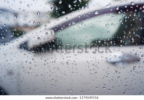 Raining outside the car while driving ,\
rainyday , raindrops on the car glass blur Rain on the car window\
with out side door mirror with traffic\
jam