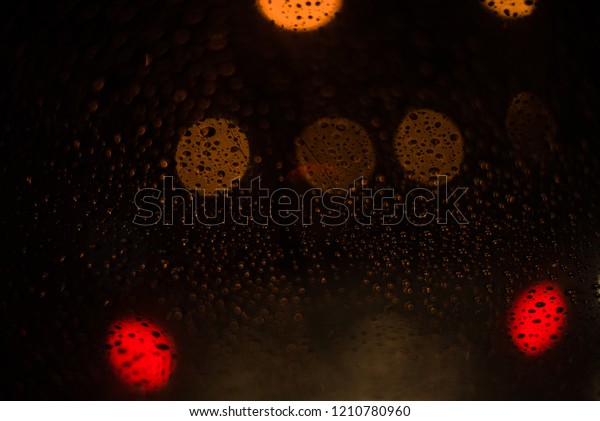 Raining season concept.Drizzle rain drop on glass with\
street colorful traffic lights at night blur bokeh abstract\
background. 