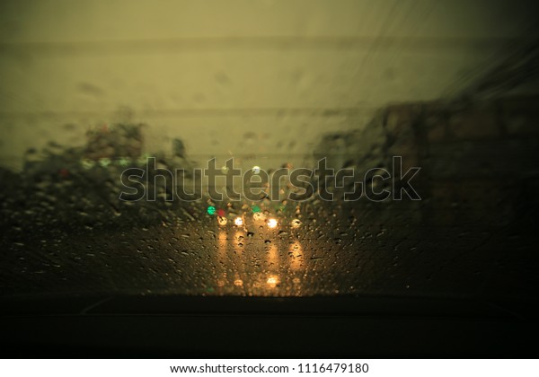 raining in the street. dark cloud and\
heavy rain. windshield of a car soak with water droplet. selective\
focus on small droplet blur car light in the\
background.