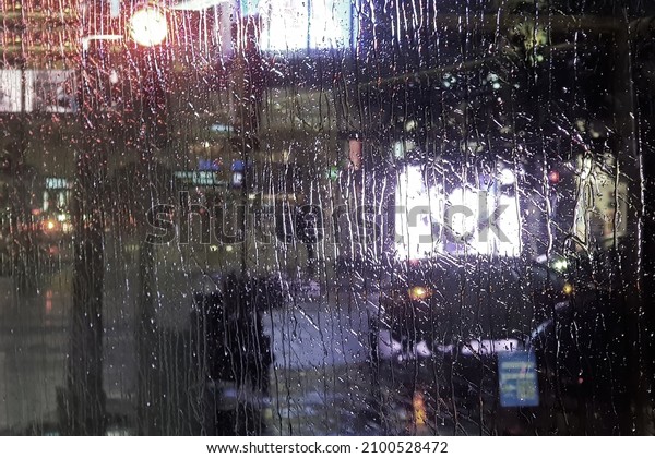 Raining in town. Night street lights reflections\
through еру bus window wet glass. Brilliant drops reflect city\
lights colors. Multi-colored blurry headlights. Cars on a wet city\
road. Misty wet night