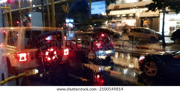 Raining in town. Night street lights reflections\
through the bus window wet glass. Brilliant drops reflect city\
lights colors. Multi-colored blurry headlights. Cars on a wet city\
road. Misty wet night