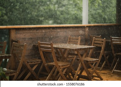 
It Rains Heavily In A Cafe, There Are No People On The Terrace Of Wood, On Which Stands A Wooden Table, Wooden Chair, On A Dark Wooden Floor