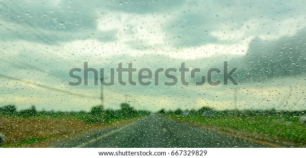 rains and water drops on glass or mirror of\
car. the road and sky and clouds. Rain is a hindrance to travel.\
Driver must careful in driving. Because water drop will make us see\
street more difficult