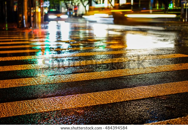 Rainstorm in the big city night, light from the
shop windows reflected on the road on which cars travel. View from
the level of asphalt