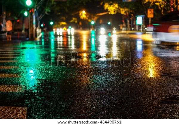 Rainstorm in the big city night, light from the\
shop windows reflected on the road on which cars travel. View from\
the level of asphalt.