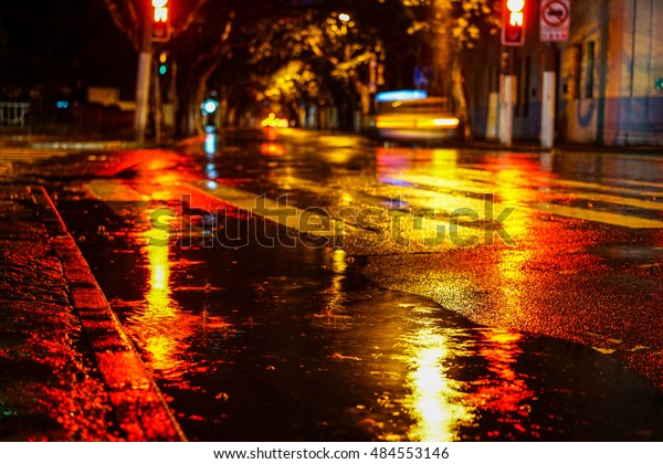 Rainstorm in the big city night, light from the\
shop windows reflected on the road on which cars travel. View from\
the level of asphalt
