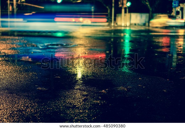 Rainstorm in the big city night, light from the
shop windows reflected on the road on which cars travel. View from
the level of asphalt