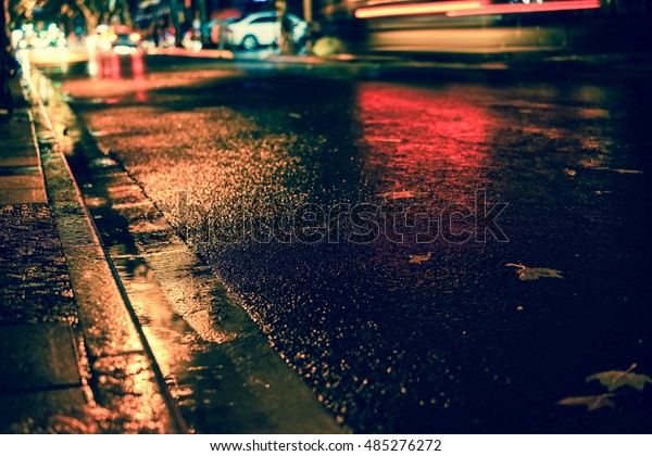 Rainstorm in the big city night, light from the\
shop windows reflected on the road on which cars travel. View from\
the level of asphalt