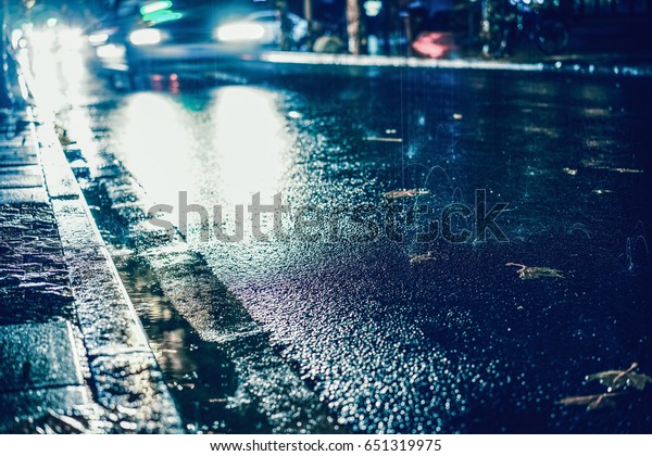 Rainstorm night in the big city, light from the\
shop windows reflected on the road on which cars travel. View from\
the level of asphalt.