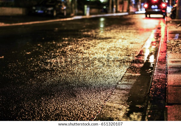 Rainstorm night in the big city, light from the
shop windows reflected on the road on which cars travel. View from
the level of asphalt.
